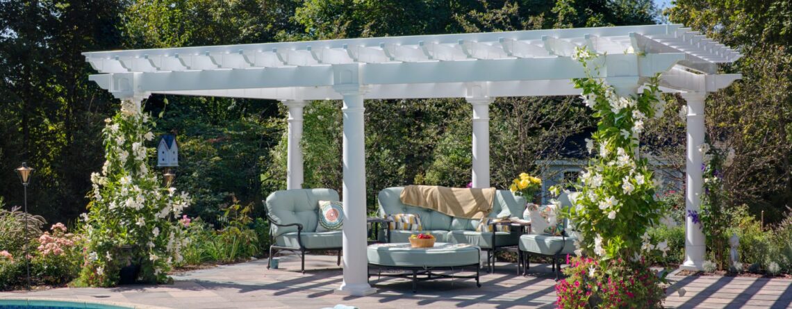 Artisan vinyl pergola with outdoor seating and vines growing up corners next to a pool.
