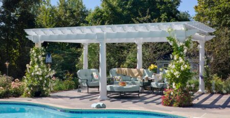 Artisan vinyl pergola with outdoor seating and vines growing up corners next to a pool.