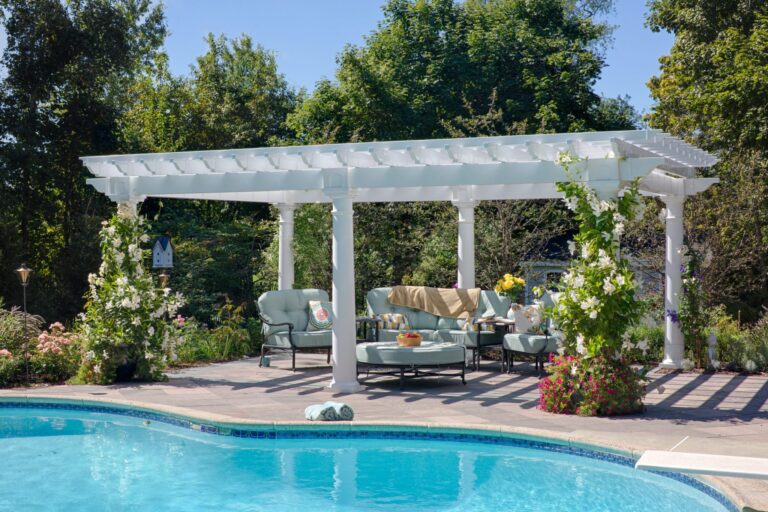 Artisan vinyl pergola with outdoor seating and vines growing up corners next to a pool.
