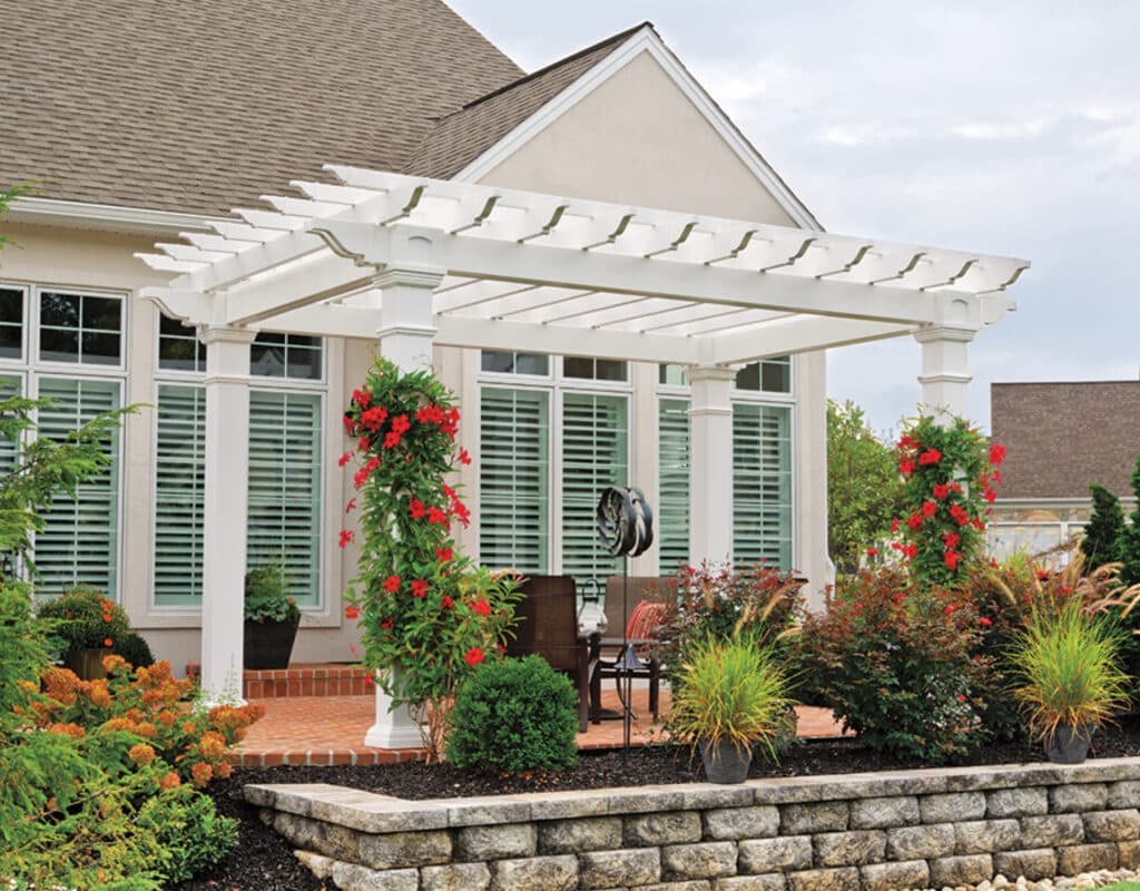 a white pergola with flowers and plants in front of a house