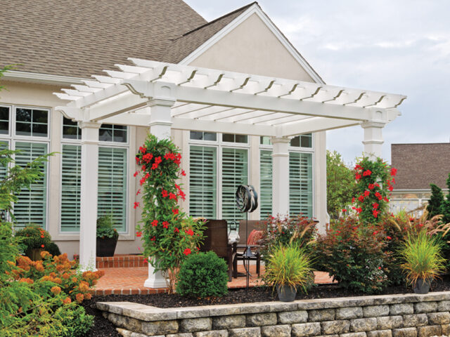 a white pergola with flowers and plants in front of a house