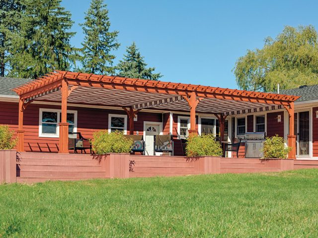 a house with a covered porch and a lawn and large outdoor wood pergola with added shade