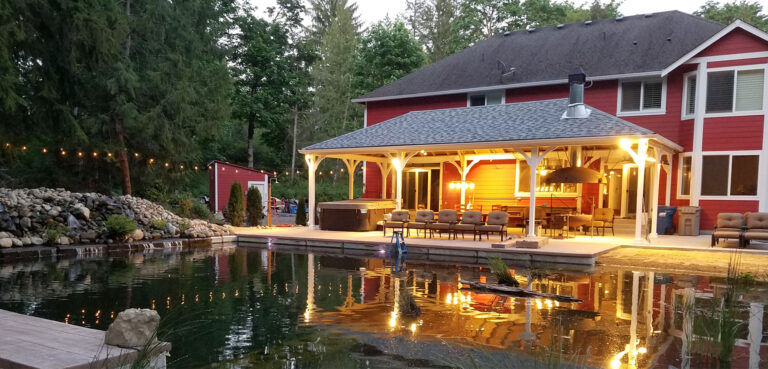 a house with a pond and a red building with a pavilion and outdoor seating